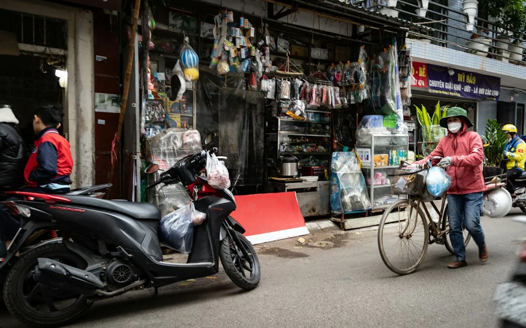 Person walking a bicycle past a Vietnamese street shop, illustrating travel alternatives to a 50cc scooter