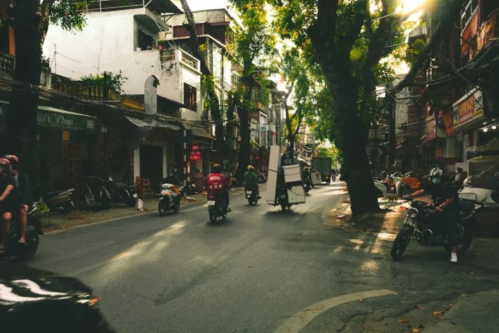 Motorräder und Passanten an einer Stadtstraße, Symbolfoto für Pendler und Studierende mit Mietroller in Hanoi
